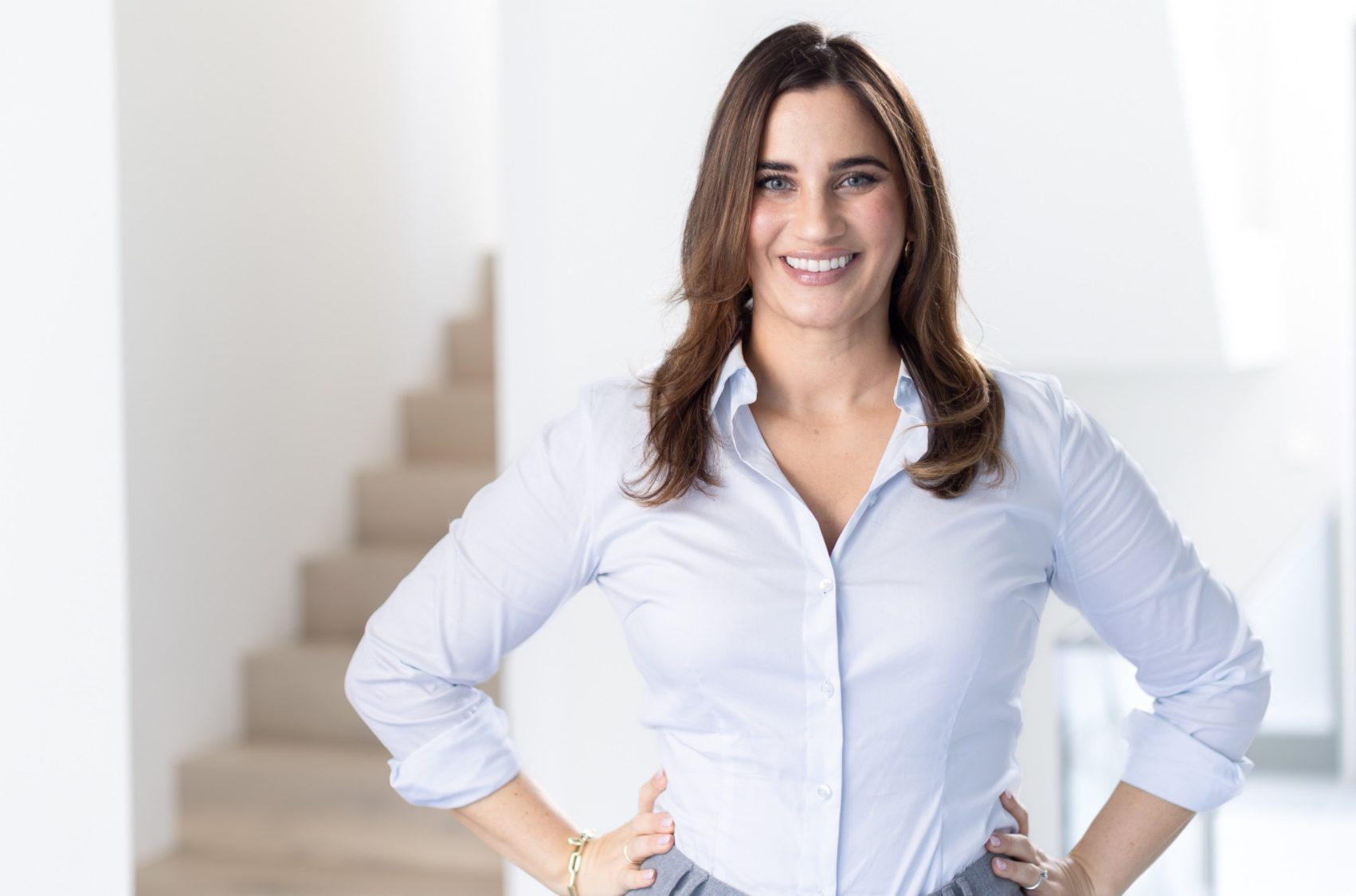 Porträt Charlotte Breidohr Lächelnde Frau mit langen, braunen Haaren in einem hellen Raum, verschränkte Arme.